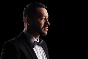 Close up profile shot of a man in a black suit and bow tie