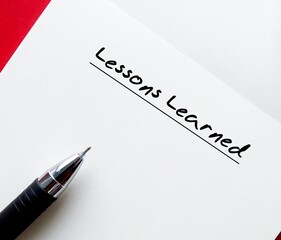 Pen on notebook writing LESSONS LEARNED, means  knowledge or understanding, positive or negative, gained by past experiences which can be advantages to future activities