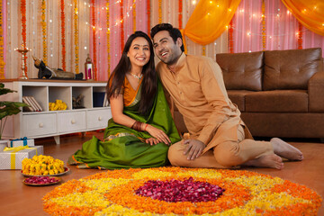 Stock image of a smiling couple making flower rangoli for diwali decoration. Young smart couple sitting together looking happy  making flower rangoli  posing for the picture  Diwali/festival celebr...