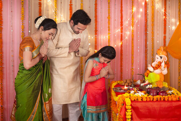 Spiritual Indian family with folded hands praying to Lord Ganesha idol - Festival. Royalty free image of a family dressed in Indian dress - Cultural show by bowing their heads to pray during Ganesh...