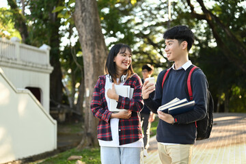 Two friendly university students are talking to each other after classes while walking in university campus outdoors