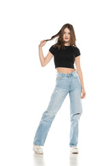 Fototapeta premium Young female model wearing ripped jeans and black shirt posing on a white background. Front view