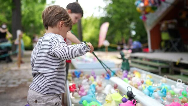 Children fishing plastic ducks at amusement park pool. Kids holding fishing rods hooking toys