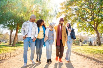 Cheerful group of friends walking outdoors in the park having fun together. Happy people talking on vacation holidays. Concept of community, youth lifestyle and friendship. High quality photo
