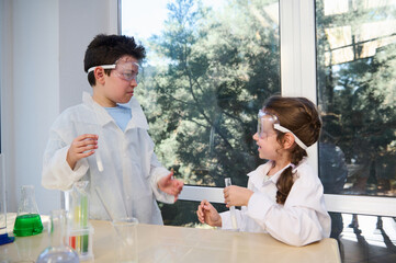 Fascinated teenage boy and primary school girl in safety goggles and lab coats. learning chemistry,...