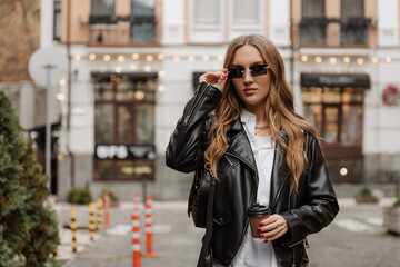 Fashionable  blonde woman model with  black leather jacket and style sunglasses walking the city...