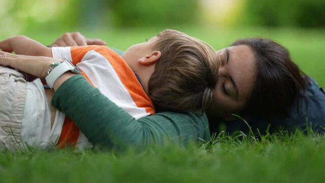 Mother lay on grass with child son. Parenting love and care. Mom laying outdoors with baby toddler