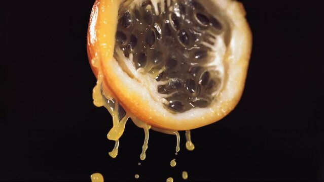 Slow Motion Macro Shot of Flowing Granadilla Juice from Halved Granadilla in black Background