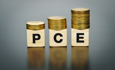 Text "PCE" (Personal Consumption Expenditure)on wood cube with coins, economic data concept.
