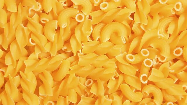 Uncooked Fusilli and Chifferi Rigati Pasta - Top View. Fat and Unhealthy Food. Classic Dry Macaroni, Slowly Rotating Background. Raw Different Macaroni Pasta Texture - Rotate Left