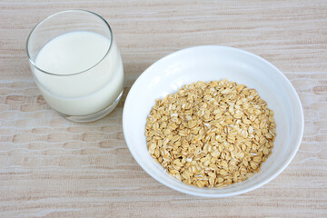 oatmeal flakes in white bowl isolated with glass of milk on beige background, close-up