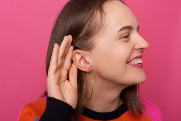 Photo of smiling satisfied woman with brown hair posing isolated over pink background, covering...
