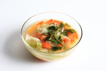 vegetable soup with chicken broth in clear bowl, isolated on white background, front view.