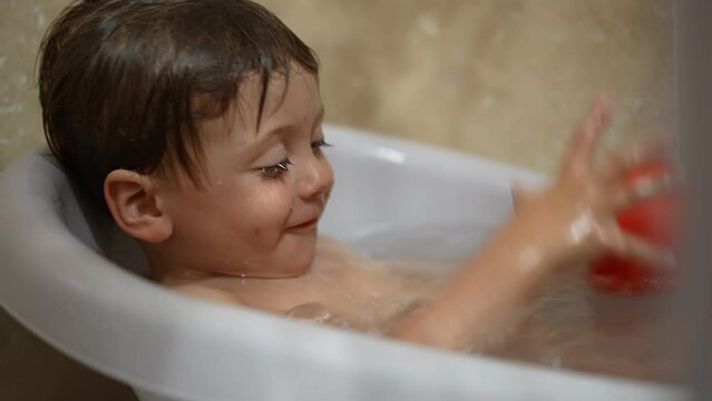 Joyful toddler inside bathtub washing body routine. Little baby boy in bath tub
