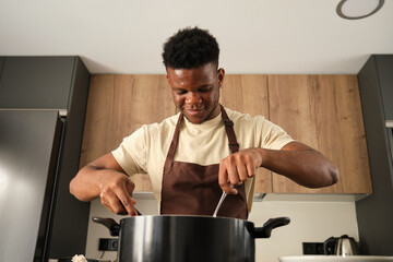 Young african man cooking in a big pot in a kitchen.