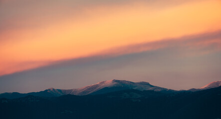 Stunning sunset with beautiful shades of orange, pink, purple and blue colors with the silhouette of a mountain range. Wallpaper, natural background with copy space.