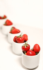 delicious sweet juicy strawberries close-up in transparent and white dishes cups on a white background