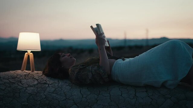 Girl reads a book on a rock with abat jour in the evening