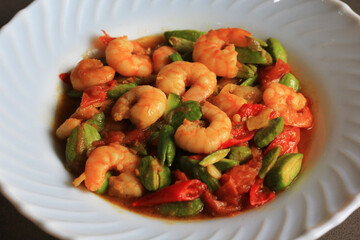 Chili prawns or Sambal Udang with petai or pete or mlanding (Parkia speciosa) cooked with mashed red chili and tomato in white plate, isolated on white background. Indonesia cuisine food, close up.