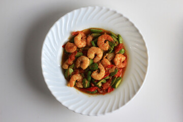Chili prawns or Sambal Udang with petai or pete or mlanding (Parkia speciosa) cooked with mashed red chili and tomato in white plate, isolated on white background. Indonesia cuisine food, top view.