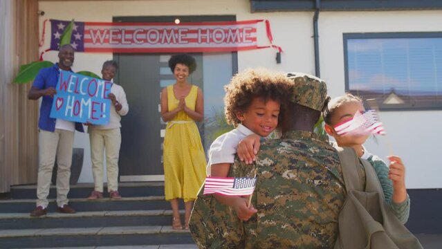 Children hugging Dad as multi-generation family welcome army father home on leave with banner - shot in slow motion