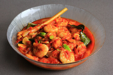 Chili prawns or Sambal Udang with petai or pete or mlanding (Parkia speciosa) cooked with mashed red chili and tomato in clear plate, with black background, front view. Indonesia cuisine food.
