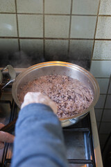 Vertical view of a pot with radish risotto and hand of an old man with vitiligo mixing it with a spatul