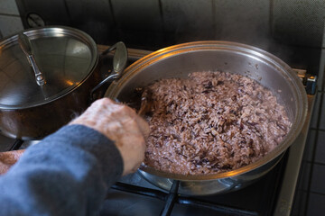 Pot with radish risotto and hand of an old man with vitiligo mixing it with a spatula.
