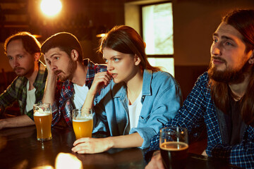 Group of young people, fans, men and women watching match at pub. Tense game moment. Losing goal