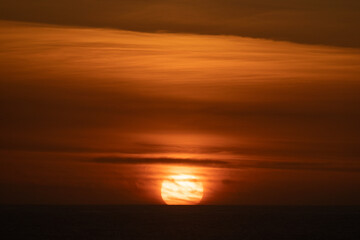 The sun setting on the horizon over the ocean with the whole sky orange