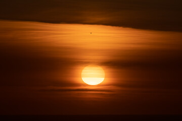 The sun setting on the horizon over the ocean with the whole sky orange