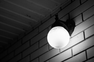 Black and white photo of a round wall lamp shining on the wall of a brick house