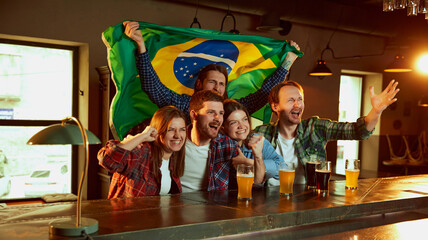 Group of young people, men and women watching football match at pub. Fans emotionally cheering up Brazil team. Success