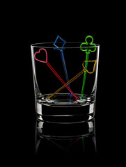 A transparent glass cup on a black background with colored transparent skewers for canapes in the form of card suits. Concept. A game. Life. Casino. Luck. Spades, clubs, diamonds, hearts.