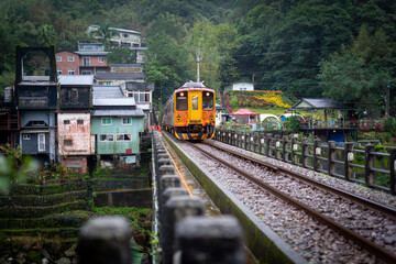 Obraz premium The yellow train is passing through a small village in the valley. Sandiaoling Station, Ruifang District, New Taipei City, Taiwan