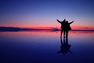 Pop art styled silhouette of happy couple on the flooding surface of Uyuni salt flats at royal blue and coral pink twilight, Bolivia, South America