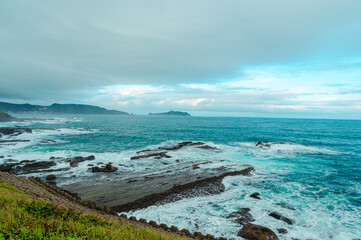 Rocky coast under blue sky and white clouds. White waves and light blue sea. Waimushan Seaside Scenic Area, Keelung, Taiwan