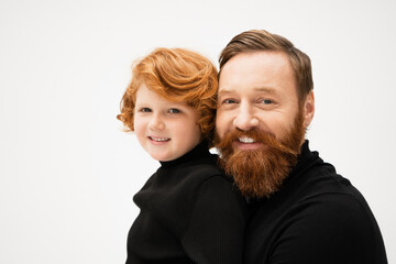 joyful bearded man with redhead grandson smiling at camera isolated on grey.