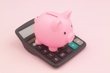 Pink piggy bank on black calculator on pink background. Saving money concept.