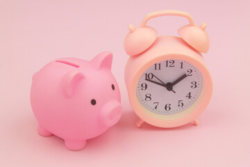 Pink alarm clock and piggy bank on pink background. Time to save money concept.