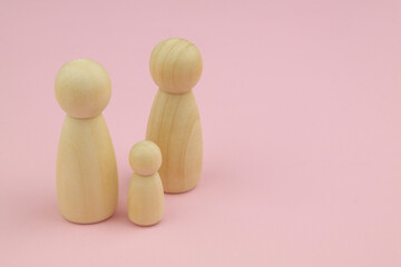 Two female wooden people figures and child figure on pink background. Copy space for text. Lesbian family concept.