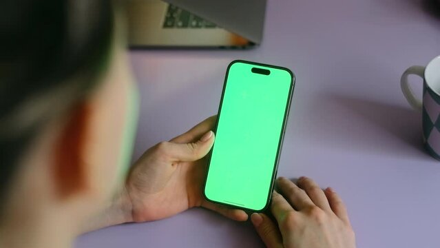 Young woman sitting on armchair at home and uses smartphone with green screen Mock-up. 4k	