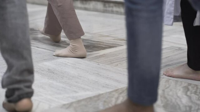 People walking barefoot on a white marble floor. Buddhist pilgrims walking and circumambulate the Mahabodhi temple in Bodh Gaya, India. Pilgrimage concept. Bare feet. People doing prostrations. 