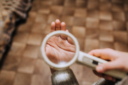 A girl, a woman holds a round magnifier with a magnifying glass and looks at the lines in the palm of her hand. Photography, palmistry concept, science.
