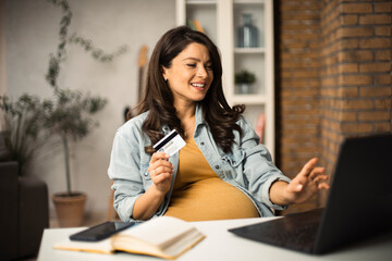 Pregnant woman shopping online at home. Happy woman with laptop and credit card..