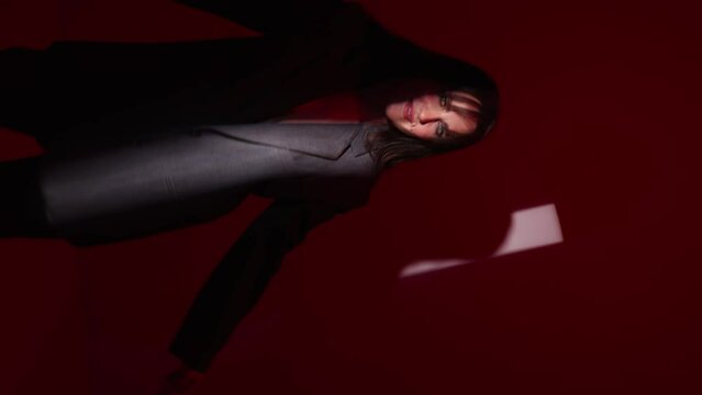 beautiful woman in suit looks into camera on red background,beam of light