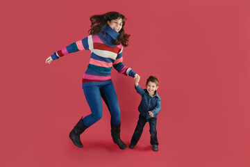 A mother with her son have fun jumping on a magenta background in studio.