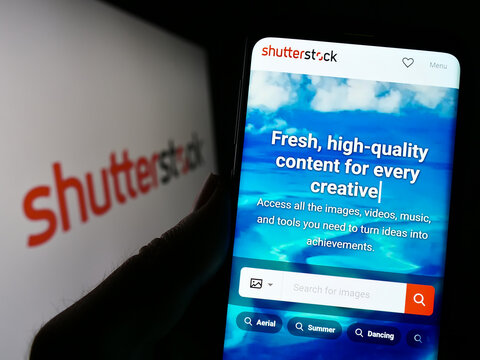 Stuttgart, Germany - 01-08-2023: Person holding cellphone with website of US stock photography company Shutterstock Inc. on screen with logo. Focus on center of phone display.