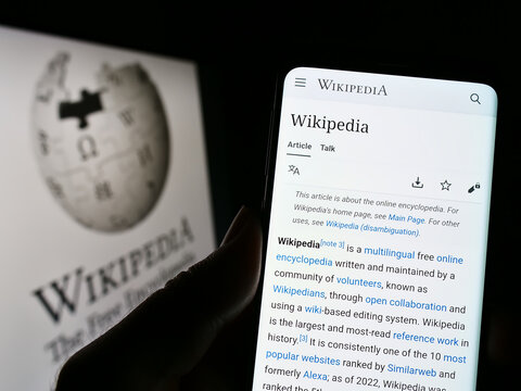 Stuttgart, Germany - 01-08-2023: Person holding cellphone with webpage of online encyclopedia Wikipedia on screen in front of logo. Focus on center of phone display.