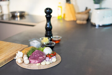 Raw wrap beef steak and variety ingredient on circle wicker plate with sauce, salt and butter in mini glass bowl on black granite kitchen counter surface.